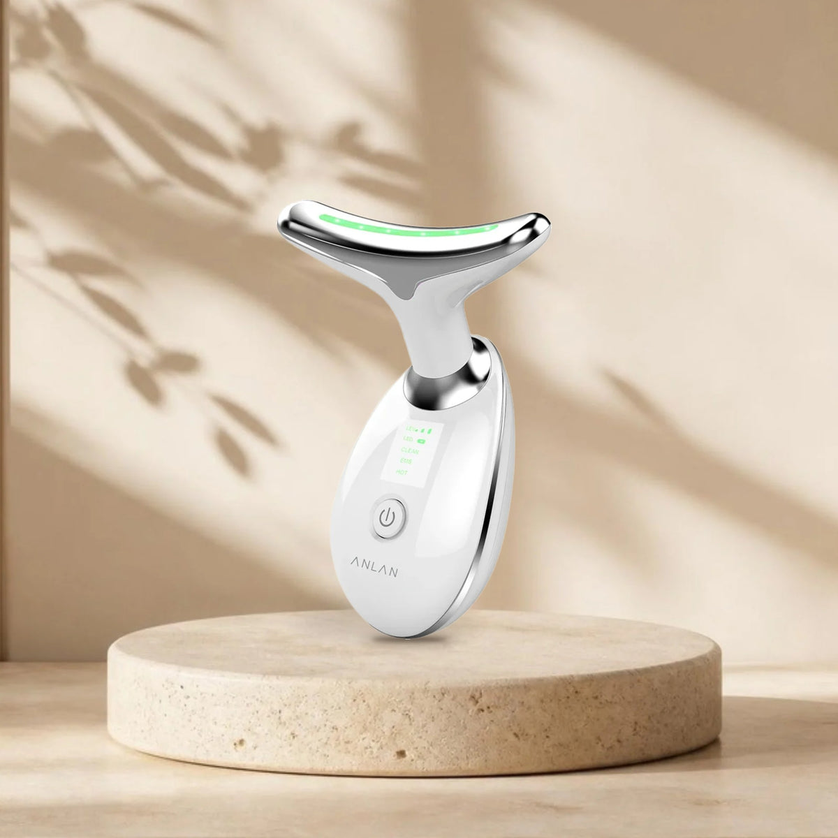 Appareil soin cou et visage ANLAN (nettoyage, EMS, chaleur) sur une plinthe en travertin, lumière naturelle et ombres de feuillage