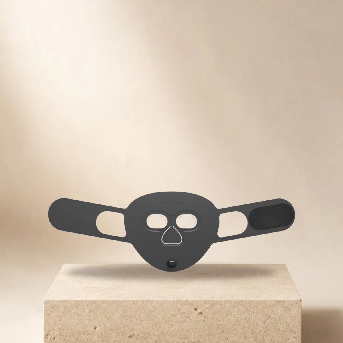 Masque LED visage Hello Face M500S noir posé sur un socle en pierre, fond beige